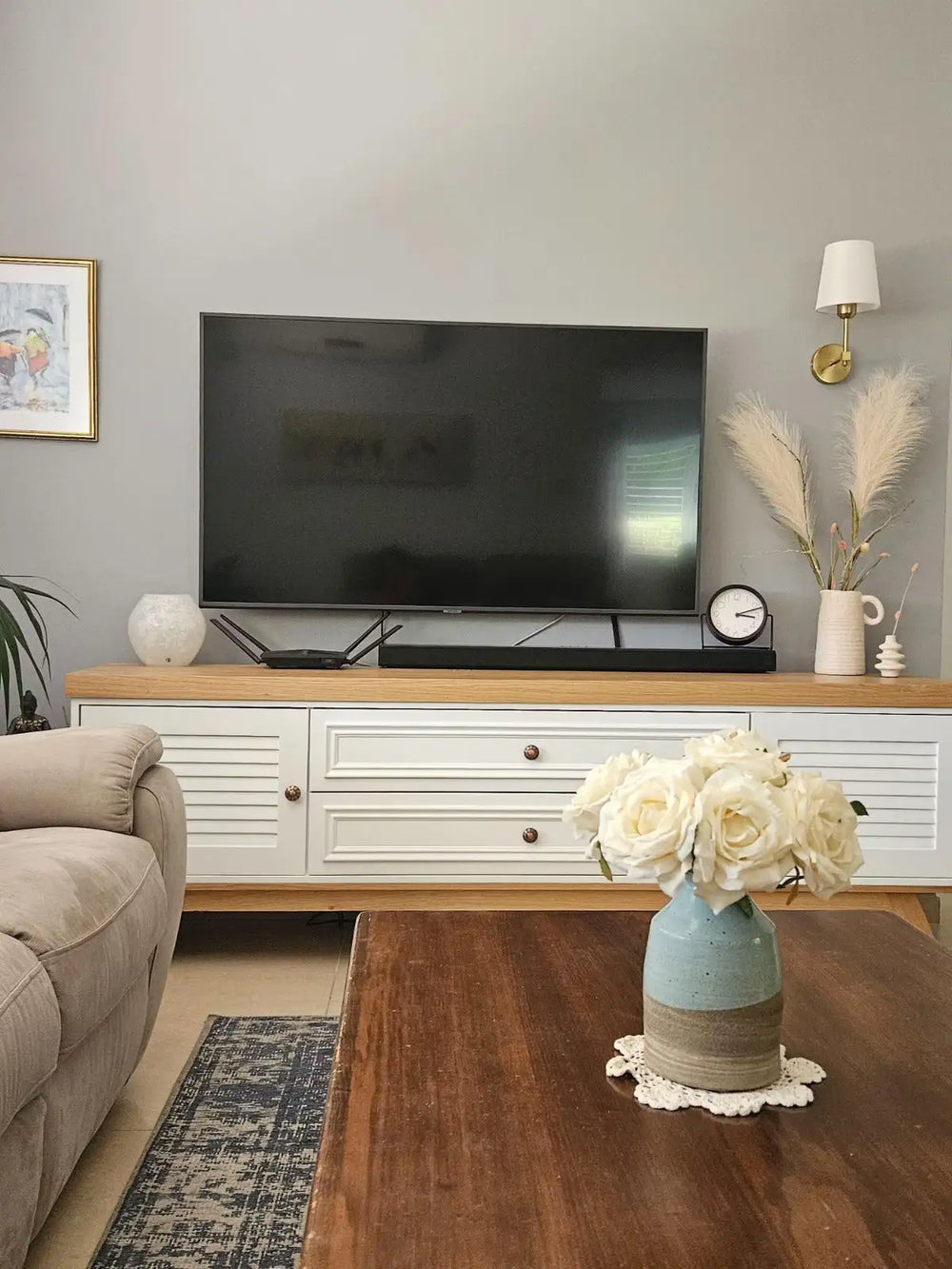 כלי חרס כחול בהיר ובז' המחזיק זר של ורדים לבנים, המונח על שולחן עץ.